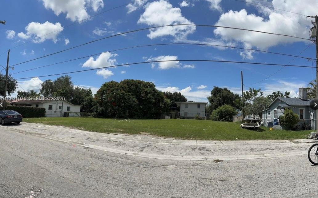 A vacant, grassy residential lot is situated between two existing houses under a cloudy sky — 1624 NW 60th St, Miami FL 33142, MIAMI, FL