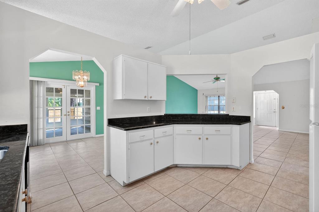 A kitchen with white cabinets, black countertops, and tile flooring, opening to a living area — 191 ROBERTS ROAD, EDGEWATER, FL