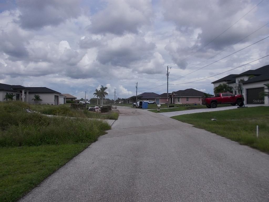 A paved residential street leads toward several houses under a cloudy sky — 538 NW 25TH TERRACE, CAPE CORAL, FL