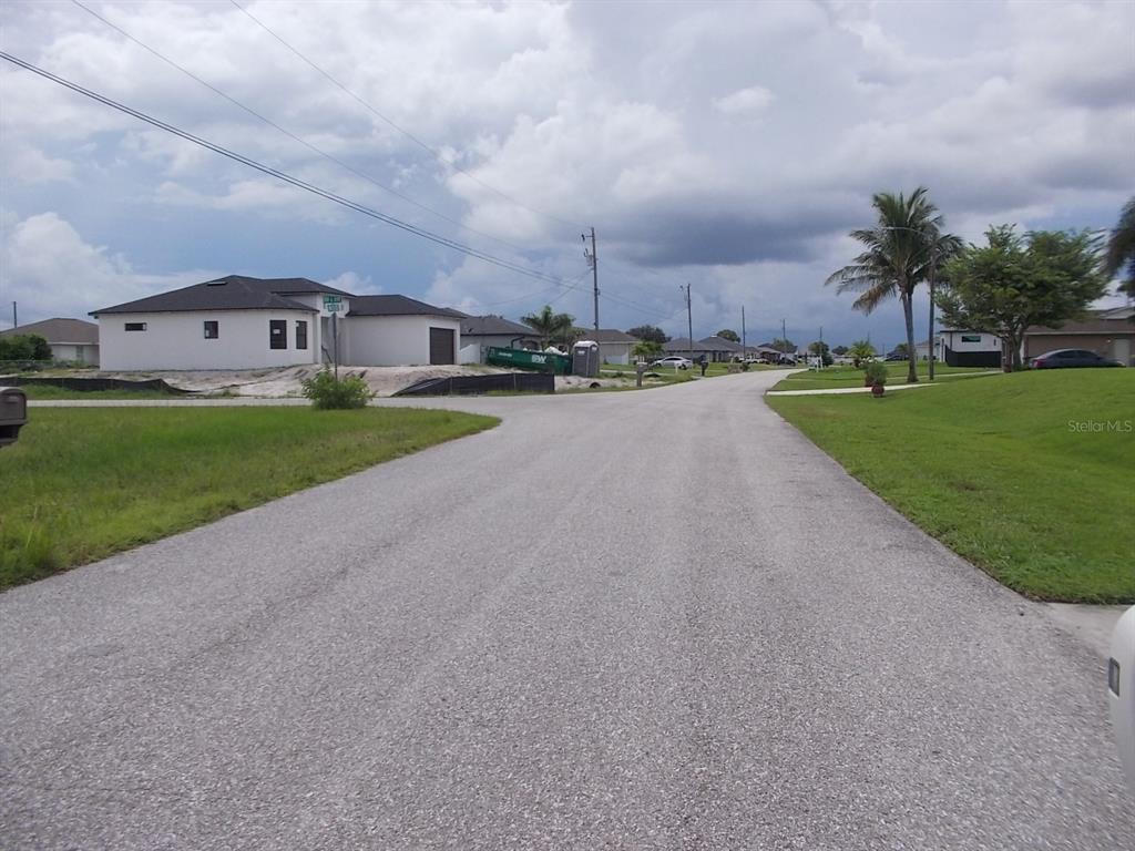 A paved street leads toward a newly constructed white house under a cloudy sky — 538 NW 25TH TERRACE, CAPE CORAL, FL