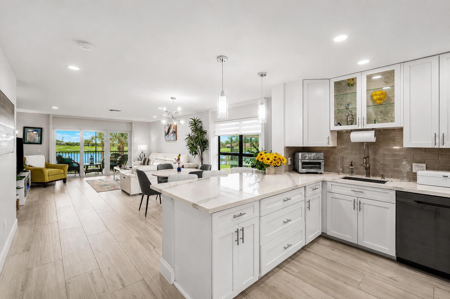 A modern kitchen with white cabinets and quartz countertops overlooks an open-concept living area — 24 Southport Lane # H, Boynton Beach FL 33436, BOYNTON BEACH, FL