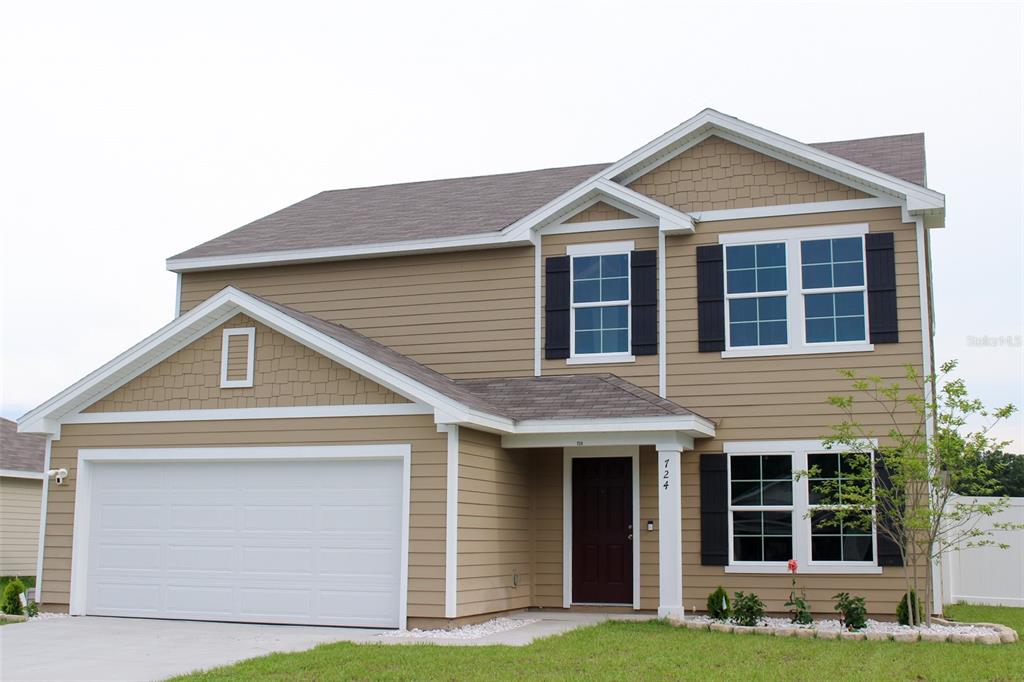 A two-story house with tan horizontal siding, a two-car garage, and a dark front door — 724 LIBERTY CIRCLE, MACCLENNY, FL