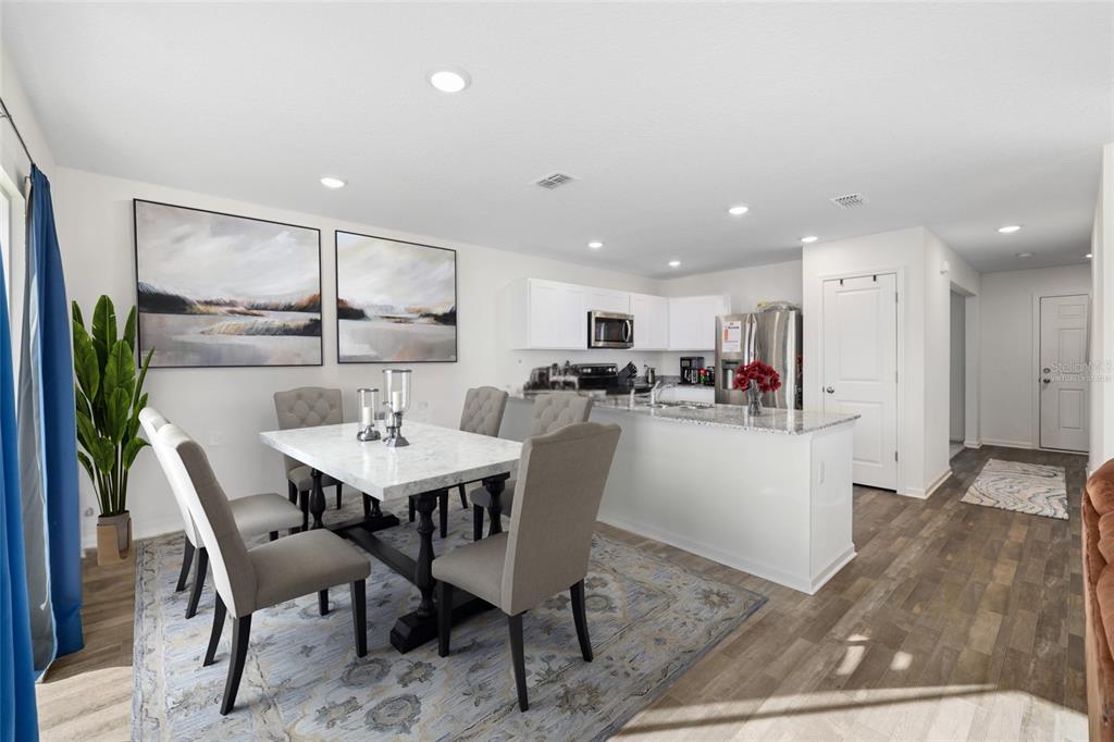 A dining area with a marble table and chairs sits adjacent to a white kitchen — 724 LIBERTY CIRCLE, MACCLENNY, FL