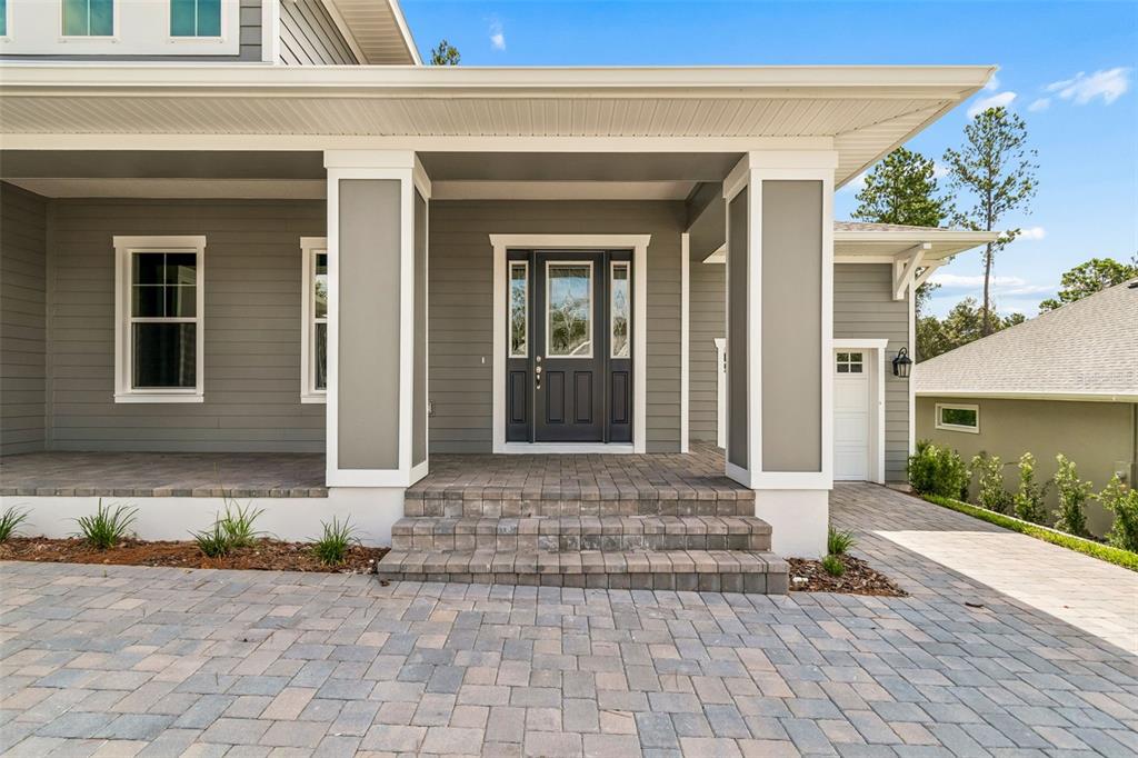 A gray house exterior features a covered porch with stone steps and a paved driveway — 4779 MAJESTIC HILLS LOOP, BROOKSVILLE, FL