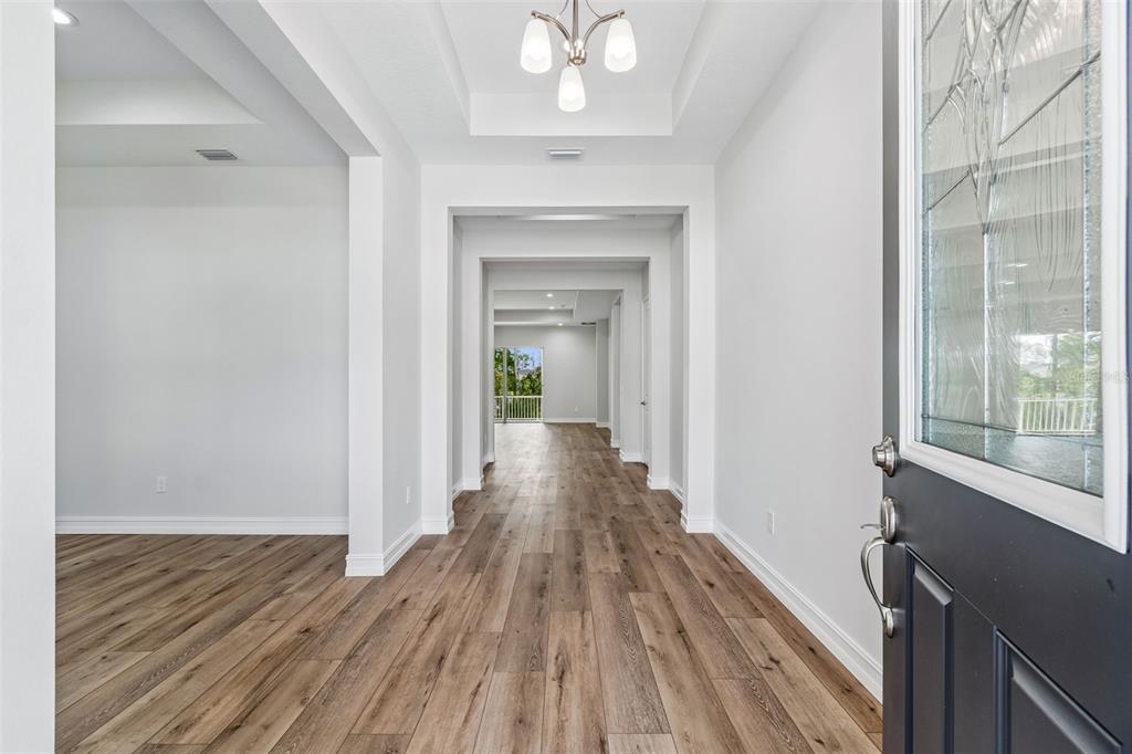 A bright entryway features wood-look flooring, a tray ceiling with a chandelier, and a glass-paneled door — 4779 MAJESTIC HILLS LOOP, BROOKSVILLE, FL