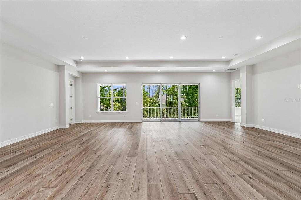 A spacious, empty room with light wood-look flooring, recessed lighting, and a sliding glass door — 4779 MAJESTIC HILLS LOOP, BROOKSVILLE, FL