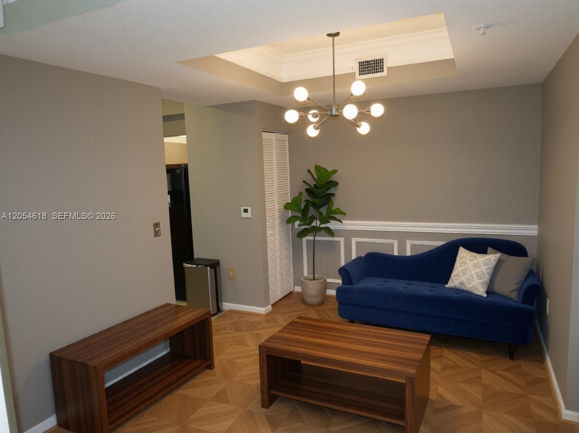 A living room features a blue sofa, wooden coffee table, and a modern chandelier — 175 Galicia Way # 0, Jupiter FL 33458, JUPITER, FL
