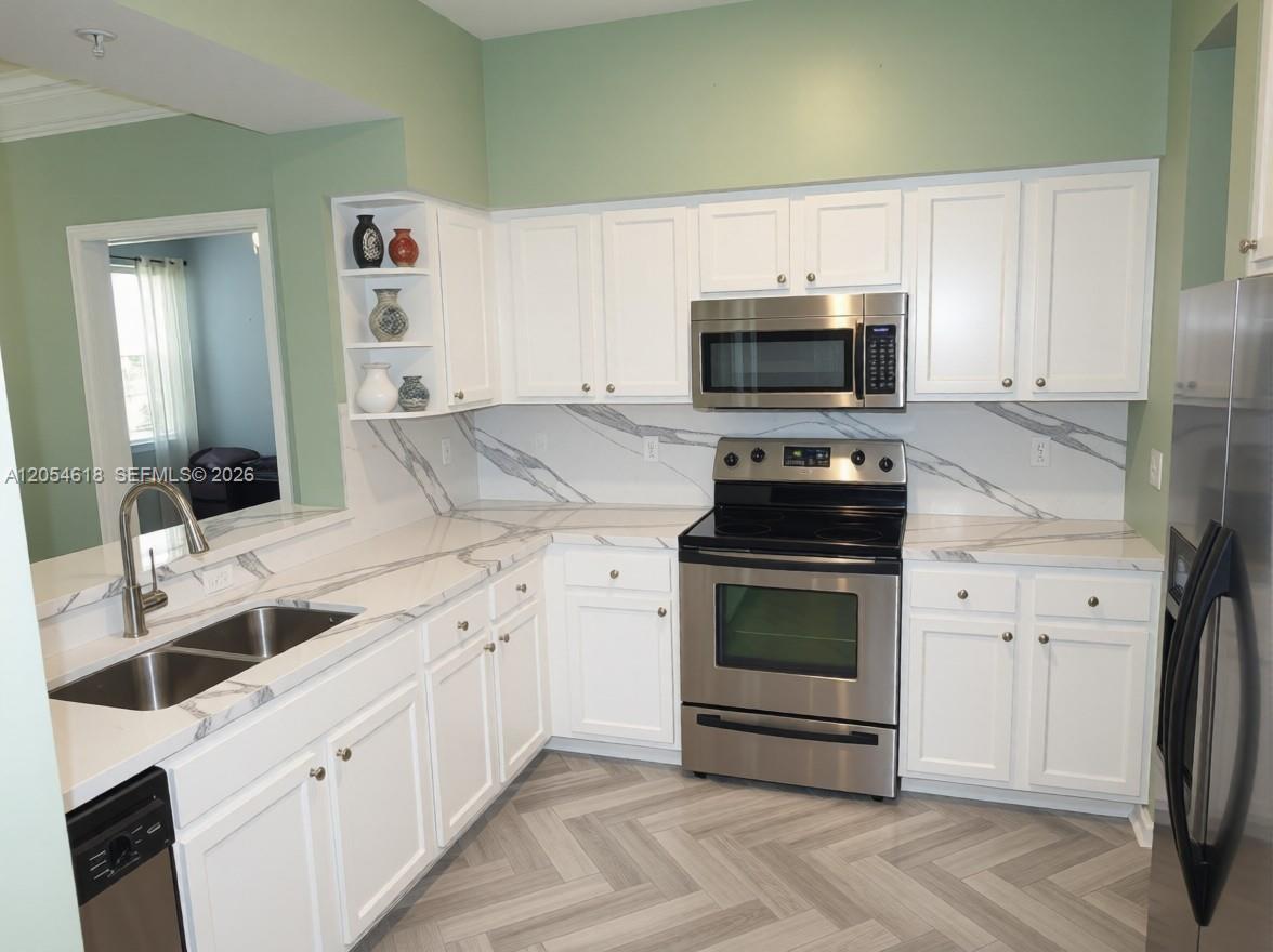 A kitchen features white cabinets, marble-patterned countertops, stainless steel appliances, and light green walls — 175 Galicia Way # 0, Jupiter FL 33458, JUPITER, FL