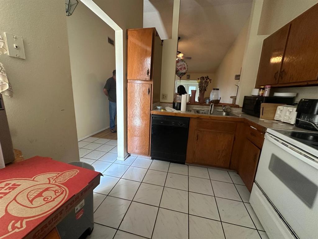 A kitchen features wood cabinets, a black dishwasher, a white stove, and white tile flooring — 3157 PHLOX DRIVE UNIT 3157, PALM HARBOR, FL