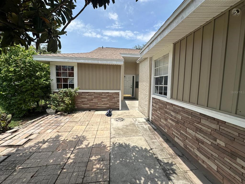 A paved patio leads to the front entrance of a house with stone and siding — 3157 PHLOX DRIVE UNIT 3157, PALM HARBOR, FL