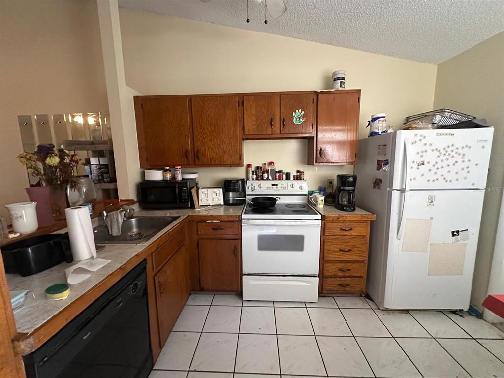 A kitchen features wood cabinets, white appliances, a tiled floor, and a double-basin sink — 3157 PHLOX DRIVE UNIT 3157, PALM HARBOR, FL