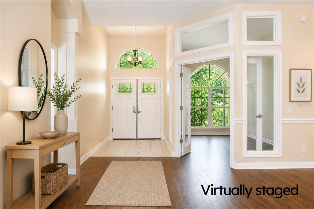 A bright foyer features a wood console table, a rug, and double doors with arched windows — 5622 GLENCREST BOULEVARD, TAMPA, FL