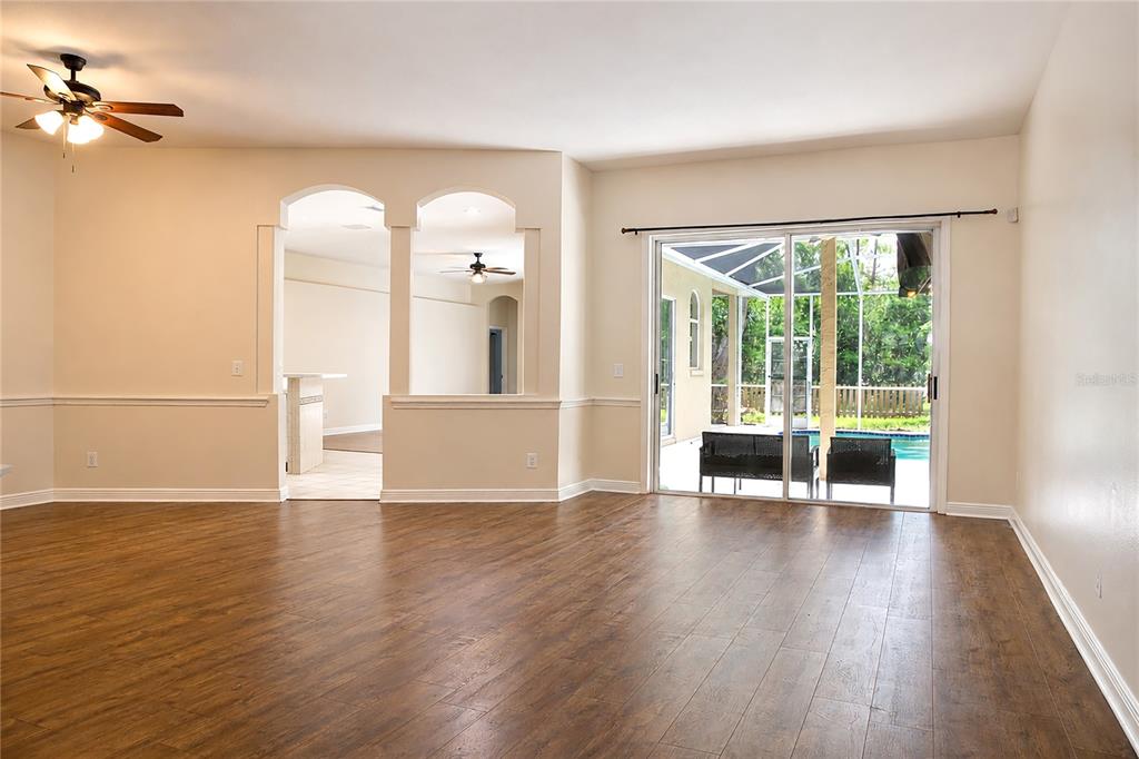 An empty living room with wood-look flooring, arched wall cutouts, and sliding glass doors — 5622 GLENCREST BOULEVARD, TAMPA, FL