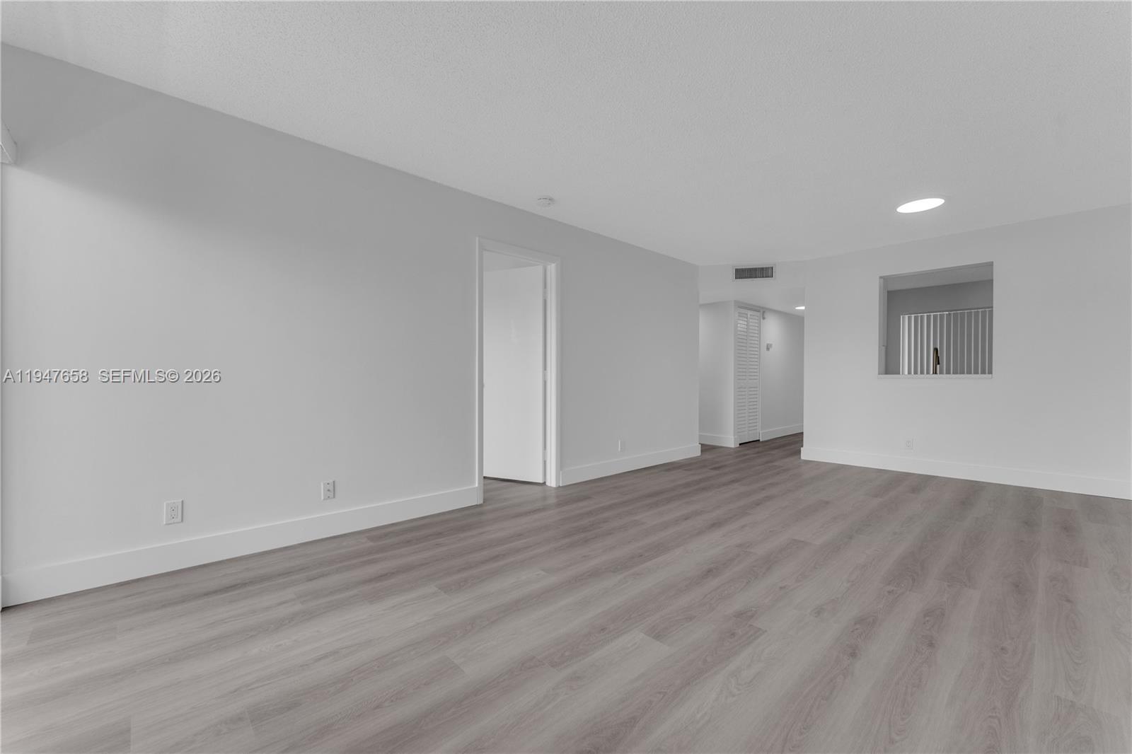 An empty room features light gray wood-look flooring, white walls, and a pass-through window — 8560 N Sherman Cir # 208, Miramar FL 33025, MIRAMAR, FL