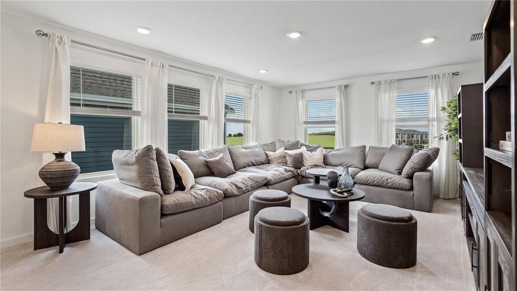 A living room features a large grey sectional sofa, three round ottomans, and multiple windows — 2713 MERCY CIRCLE, CLERMONT, FL
