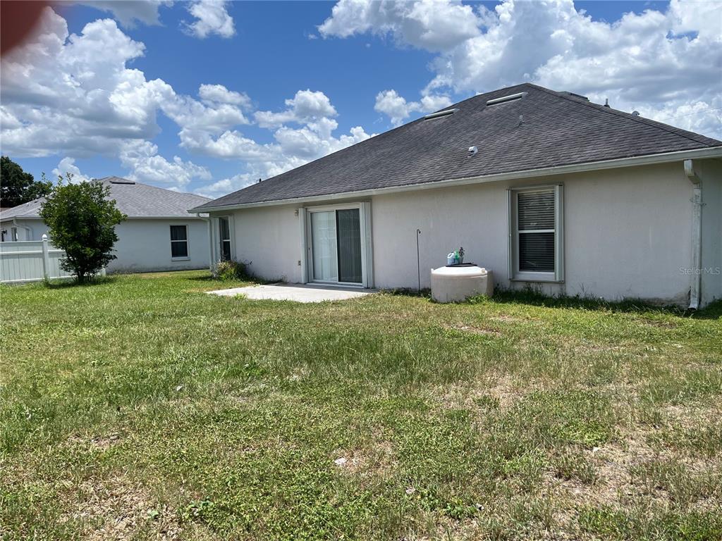 The backyard of a single-story house features a concrete patio, sliding glass doors, and lawn — 856 FRANCONVILLE COURT, KISSIMMEE, FL