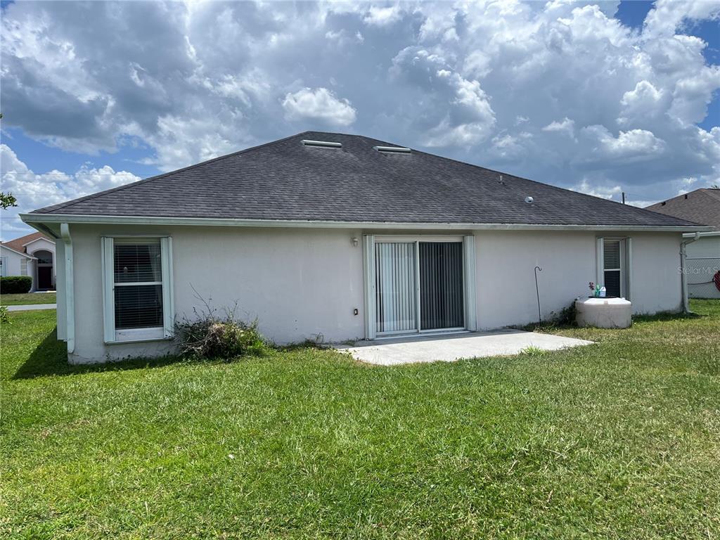 The rear exterior of a single-story house features a concrete patio and sliding glass doors — 856 FRANCONVILLE COURT, KISSIMMEE, FL