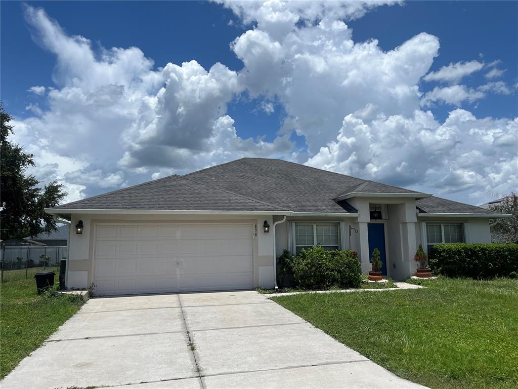 A single-story house with a two-car garage, light-colored stucco walls, and a blue front door — 856 FRANCONVILLE COURT, KISSIMMEE, FL