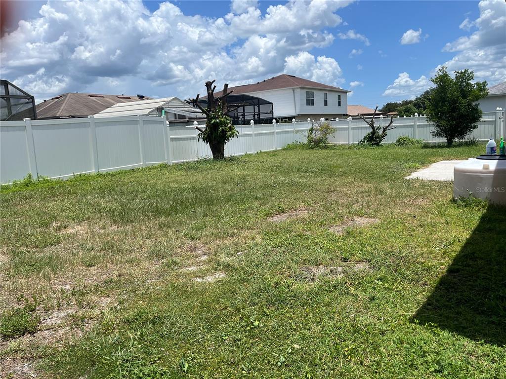 A grassy backyard features a white vinyl fence, a large water tank, and trees — 856 FRANCONVILLE COURT, KISSIMMEE, FL