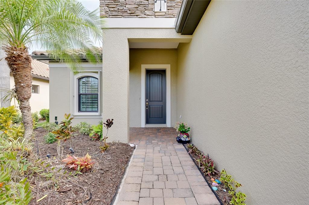 A paved walkway leads to the dark front door of a stucco home with stone accents — 228 ACERNO DRIVE, NOKOMIS, FL