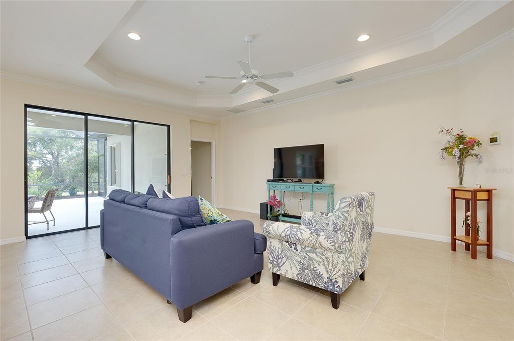 A living room features a blue sofa, patterned armchair, television console, and sliding glass doors — 228 ACERNO DRIVE, NOKOMIS, FL