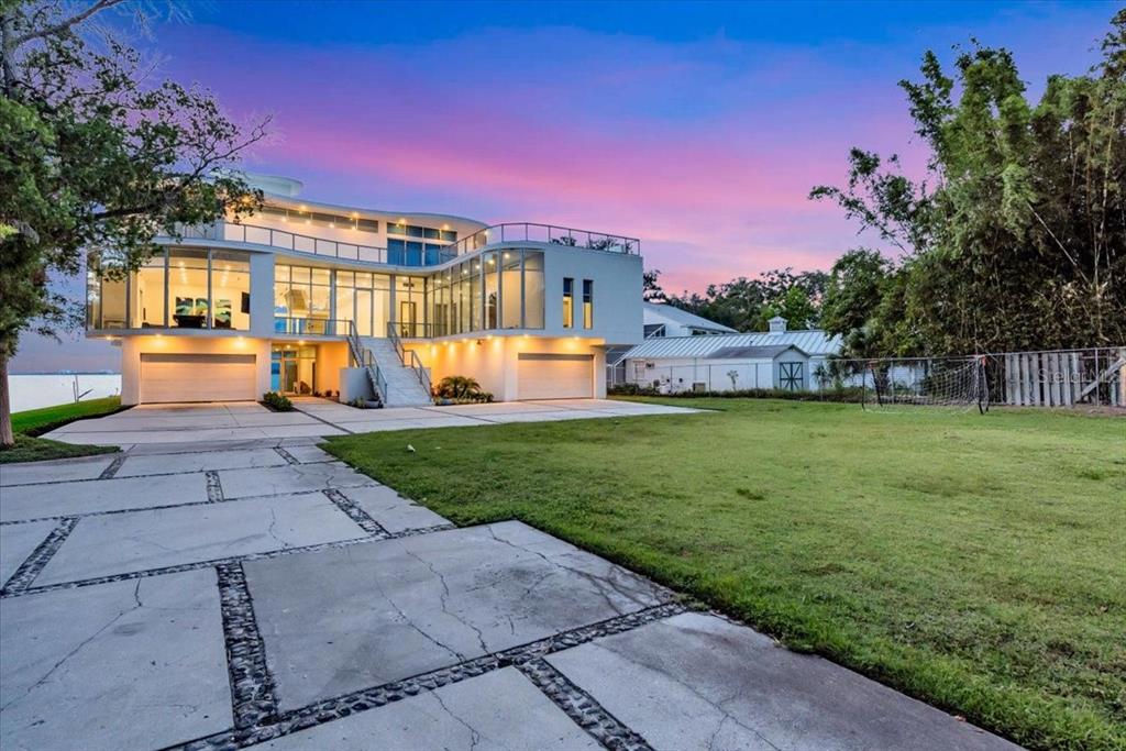 A modern, multi-story white house with large glass windows and a concrete driveway at sunset — 4035 BAY SHORE ROAD, SARASOTA, FL