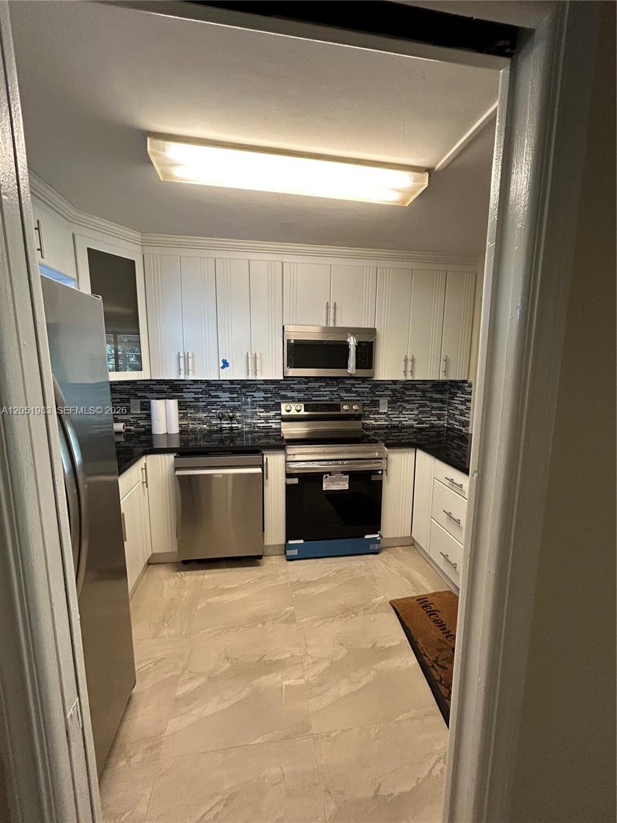 A kitchen features white cabinetry, stainless steel appliances, black countertops, and a tiled floor — 9461 Evergreen Pl # 303, Davie FL 33324, DAVIE, FL