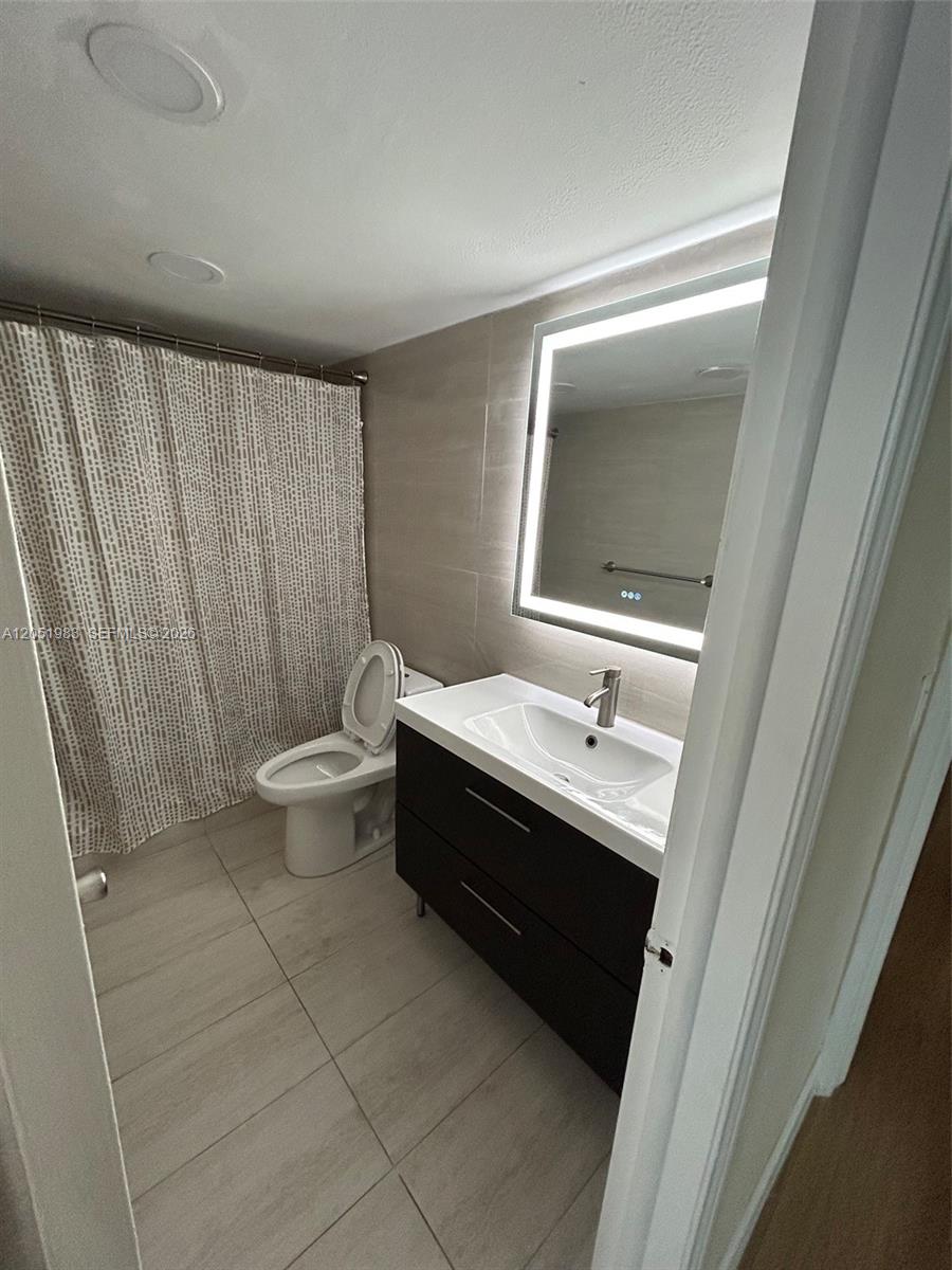A bathroom features a dark wood vanity, a backlit mirror, and a patterned shower curtain — 9461 Evergreen Pl # 303, Davie FL 33324, DAVIE, FL