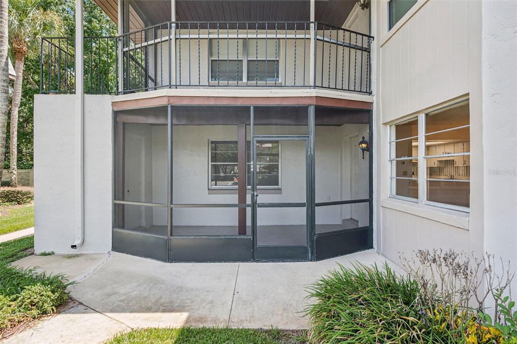 A ground-level screened-in patio sits beneath a second-story balcony with a metal railing — 93 WINDTREE LANE UNIT 102, WINTER GARDEN, FL