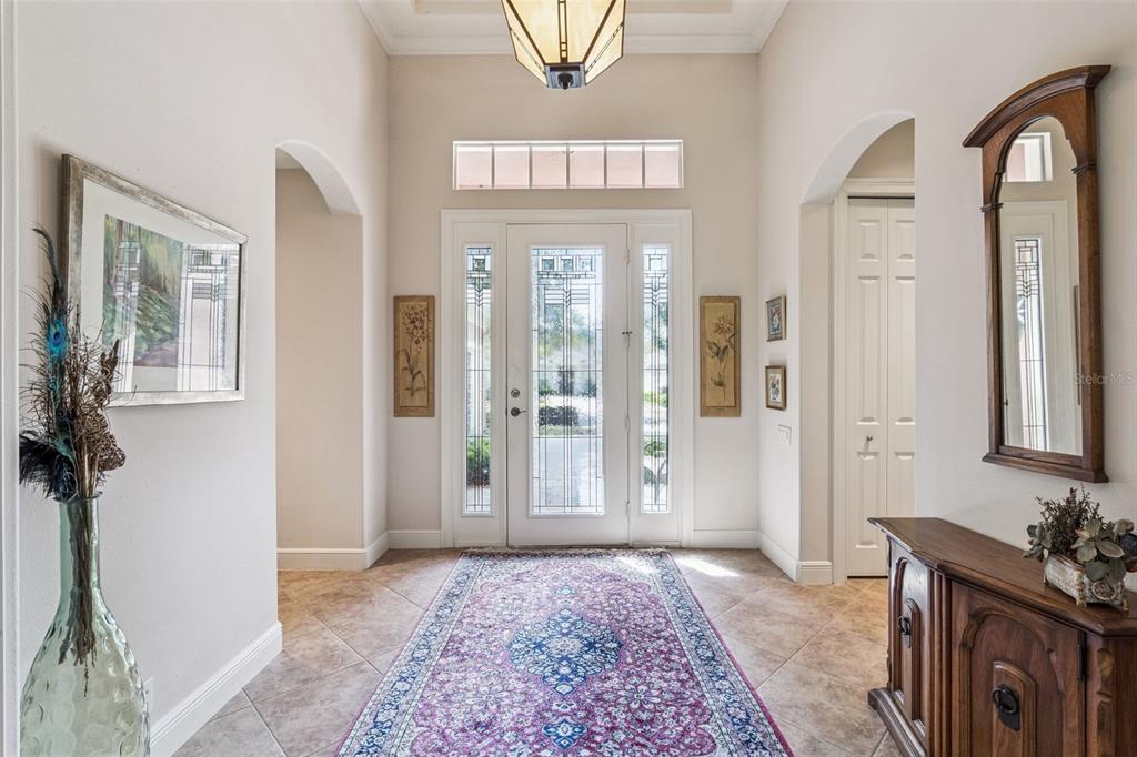 A bright entryway features a patterned rug, tile flooring, a glass-paneled door, and arched doorways — 322 BELLINGRATH TERRACE, DELAND, FL