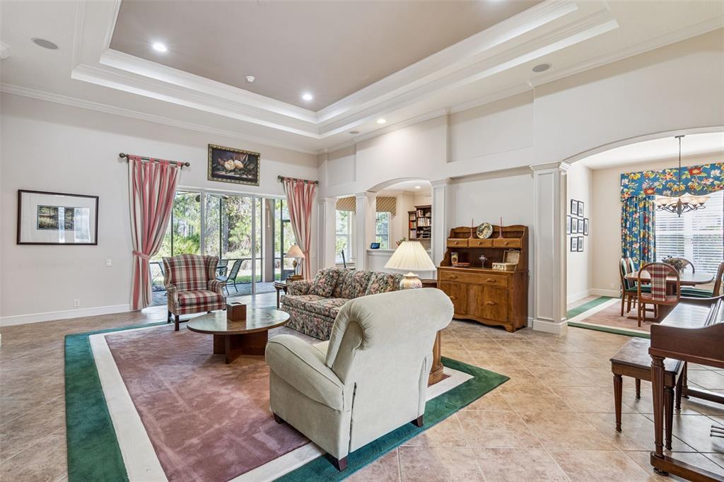 A spacious living room with tile floors, a tray ceiling, and a dining area beyond — 322 BELLINGRATH TERRACE, DELAND, FL