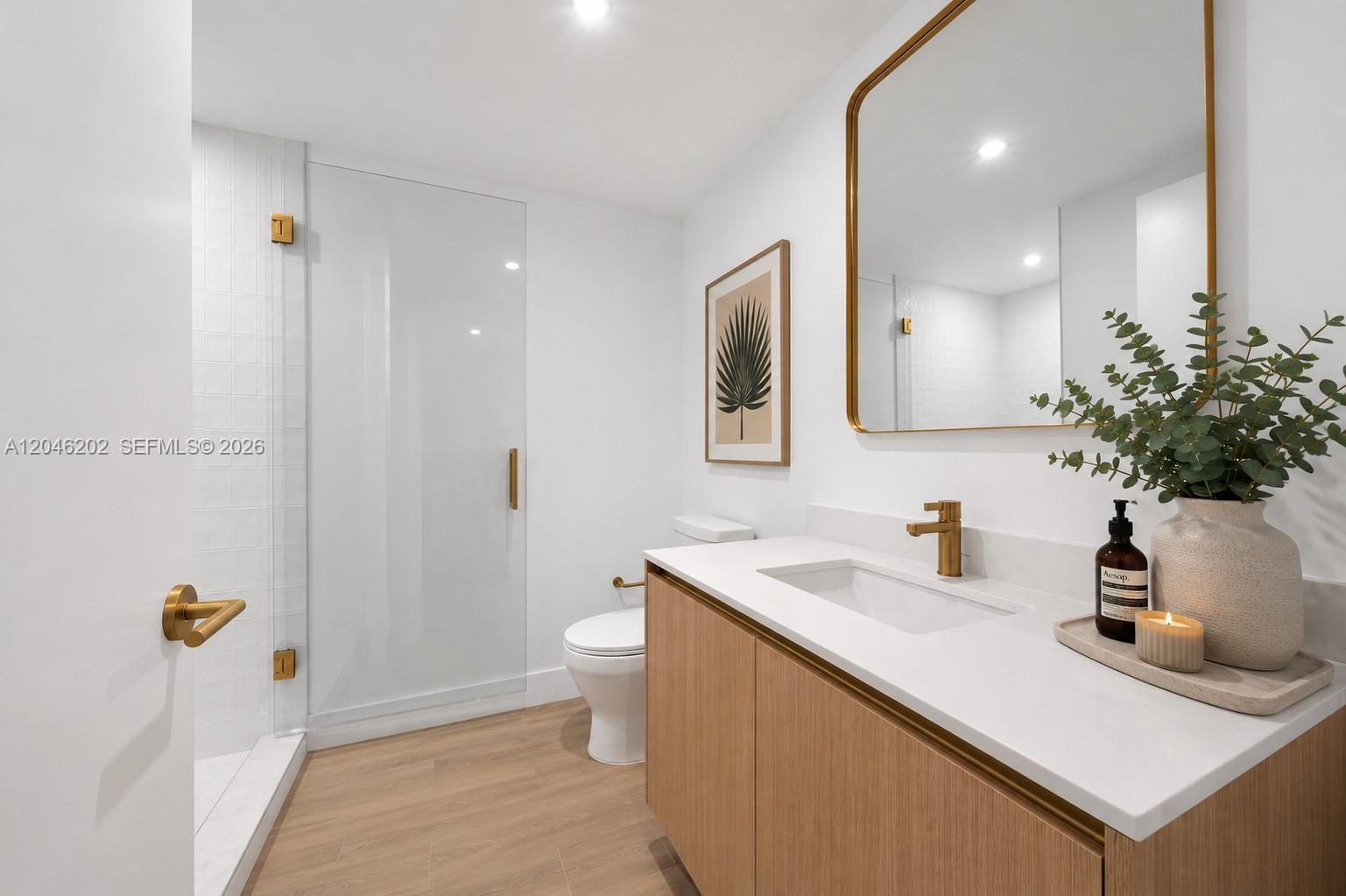 A modern bathroom features a wood vanity, white countertop, gold fixtures, and a glass shower — 90 NE 32nd # 404, Miami FL 33127, MIAMI, FL