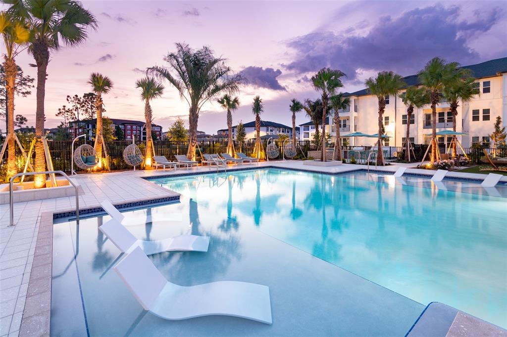 A swimming pool with lounge chairs sits in front of a multi-story apartment building at sunset — 100 WINDFLOWER LANE UNIT C1, DAYTONA BEACH, FL