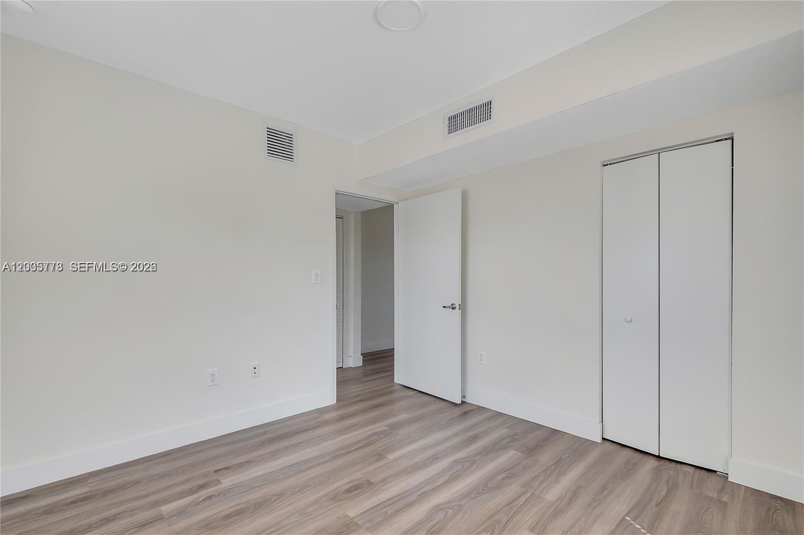 An empty bedroom features light-colored walls, wood-look flooring, a closet, and an open doorway — 1710 NW 1st Ct # 15, Miami FL 33136, MIAMI, FL