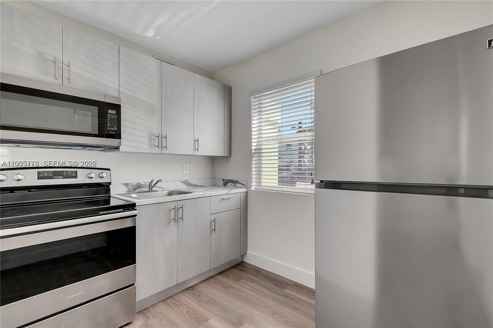 A small kitchen features stainless steel appliances, light gray cabinetry, and wood-look flooring — 1710 NW 1st Ct # 15, Miami FL 33136, MIAMI, FL