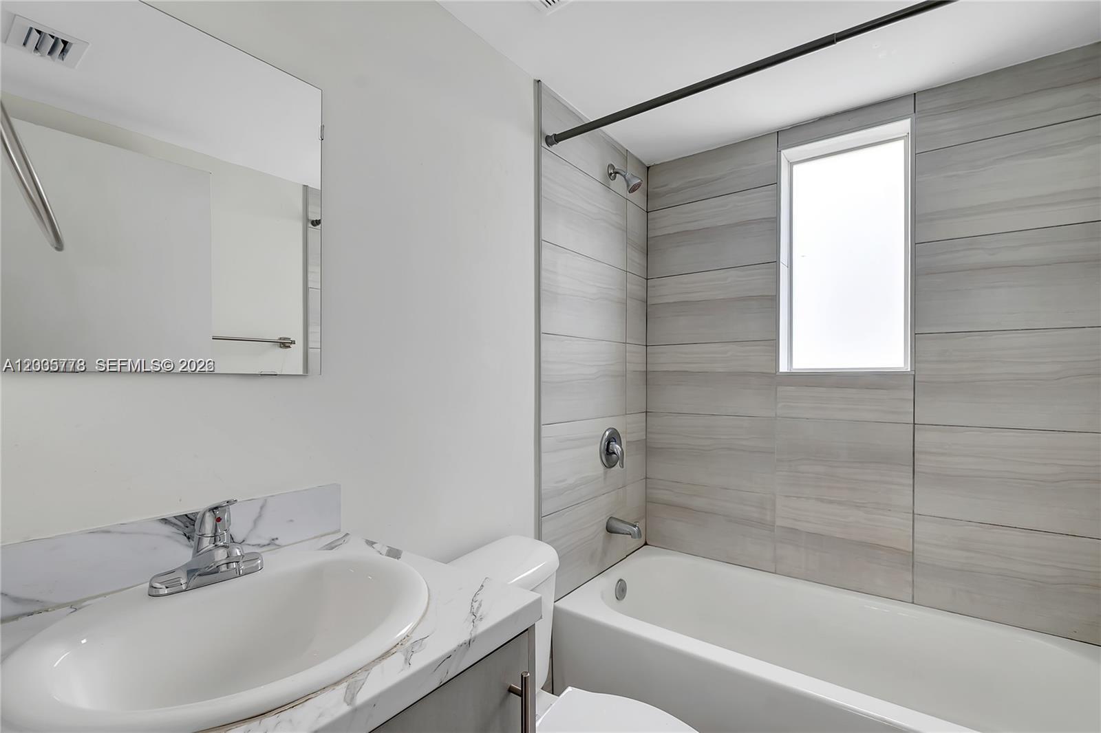 A bathroom features a vanity with a marble-look countertop, a toilet, and a tiled tub-shower — 1710 NW 1st Ct # 15, Miami FL 33136, MIAMI, FL