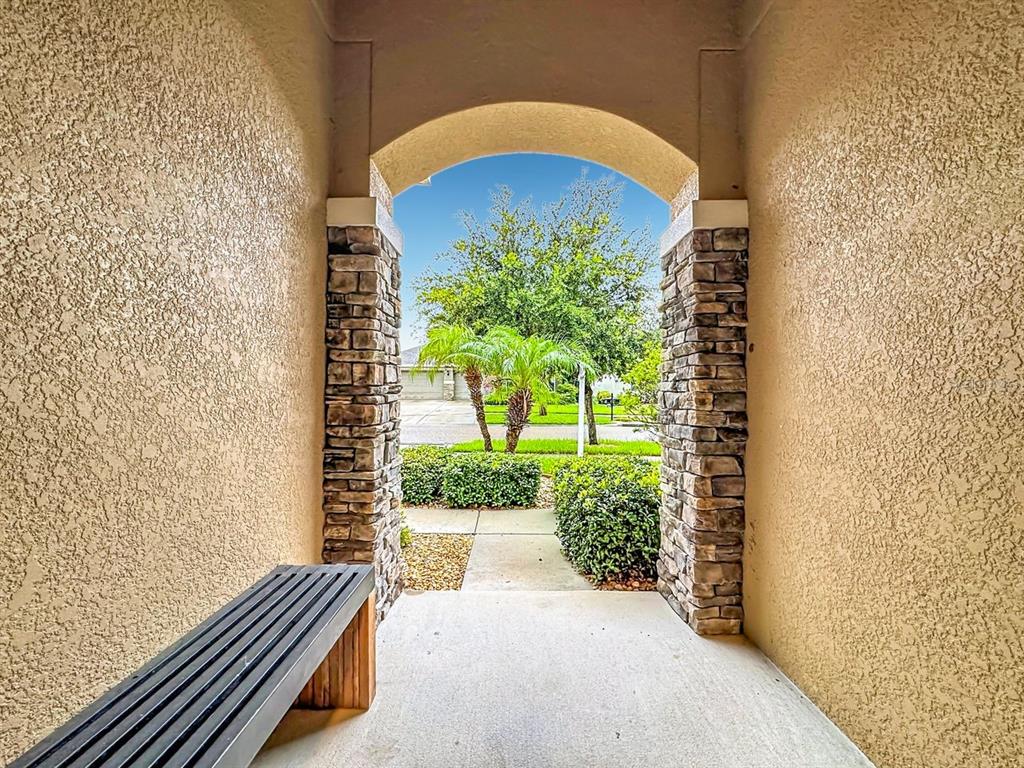 A covered entryway features a stone-accented arched opening, a concrete floor, and a wooden bench — 10445 FLAGSTAFF FALLS AVENUE, RIVERVIEW, FL