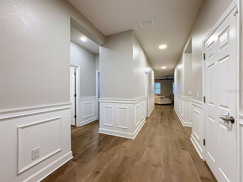 A hallway with wood-look flooring, white wainscoting, and recessed lighting leads toward a living area — 10445 FLAGSTAFF FALLS AVENUE, RIVERVIEW, FL