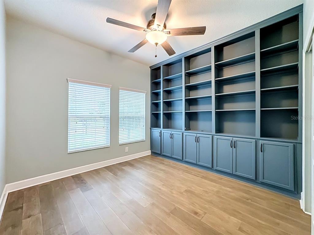 A room with light wood floors, two windows, and a large built-in blue bookshelf — 10445 FLAGSTAFF FALLS AVENUE, RIVERVIEW, FL