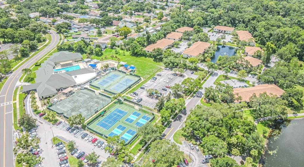 An aerial view shows a community center with tennis courts, a pool, and surrounding buildings — 3345 CRYSTAL COURT E UNIT H, PALM HARBOR, FL