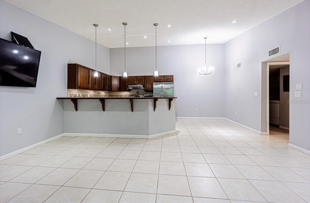 A kitchen with dark wood cabinets and a breakfast bar overlooks a tiled living area — 3345 CRYSTAL COURT E UNIT H, PALM HARBOR, FL