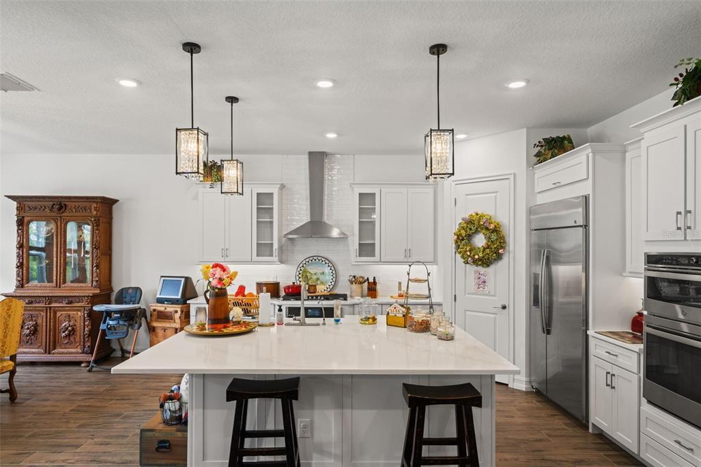A white kitchen features a large center island, stainless steel appliances, and dark wood flooring — 6170 MARSH TRAIL DRIVE, ODESSA, FL