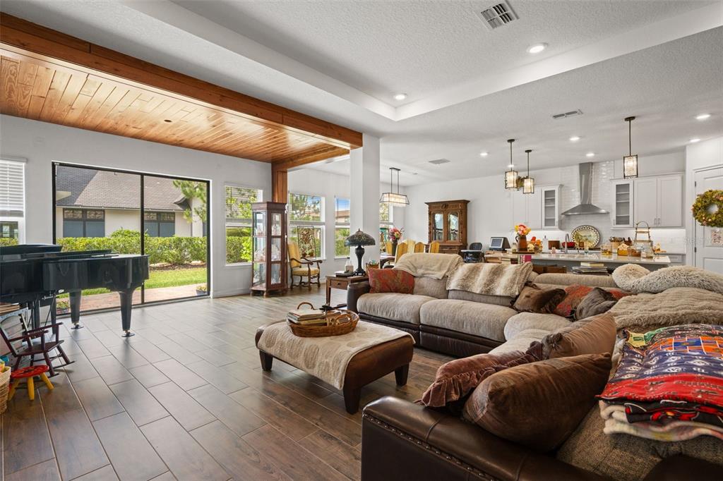 A spacious open-concept living room with wood-look tile floors, a grand piano, and kitchen access — 6170 MARSH TRAIL DRIVE, ODESSA, FL