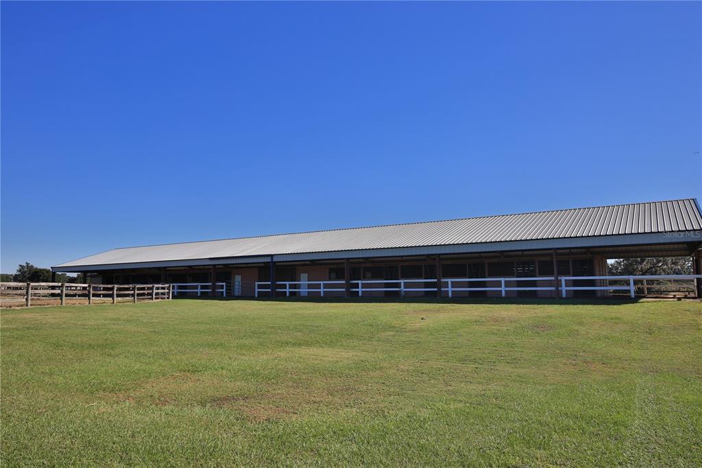 A long, single-story horse stable with a metal roof sits beside a fenced grassy pasture — 2711 SW 125TH AVENUE, OCALA, FL