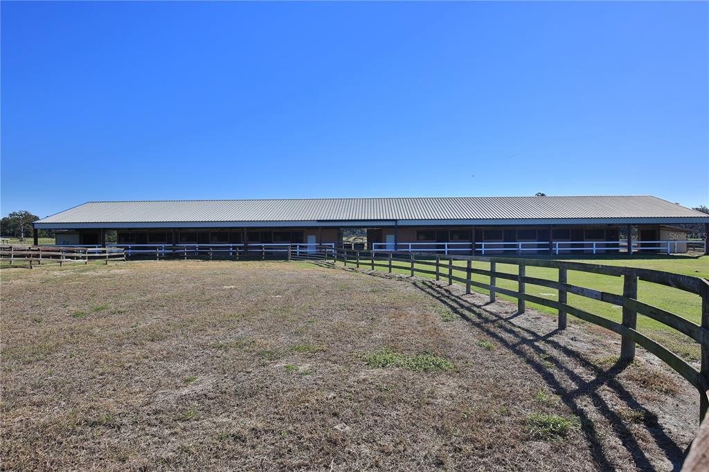 A long, single-story stable building sits behind a wooden fence in a grassy field — 2711 SW 125TH AVENUE, OCALA, FL
