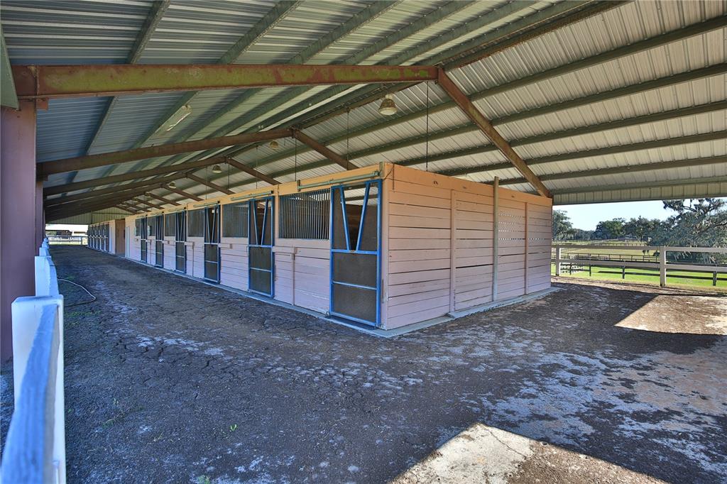 A covered outdoor horse stable features multiple stalls with blue metal doors and wooden walls — 2711 SW 125TH AVENUE, OCALA, FL