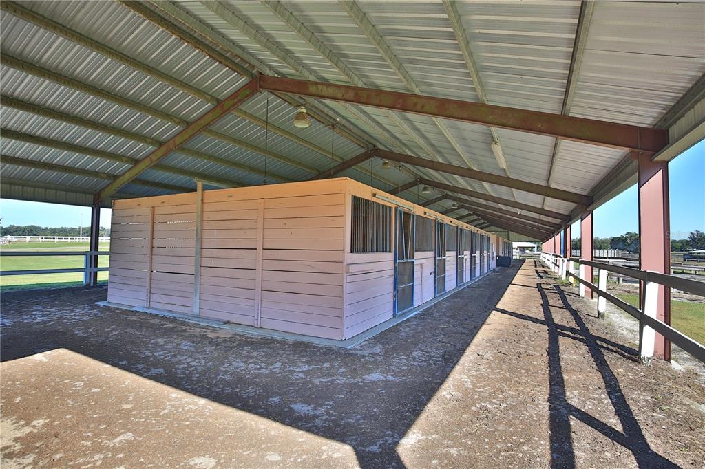 An outdoor horse stable with a metal roof and multiple stalls under a covered walkway — 2711 SW 125TH AVENUE, OCALA, FL