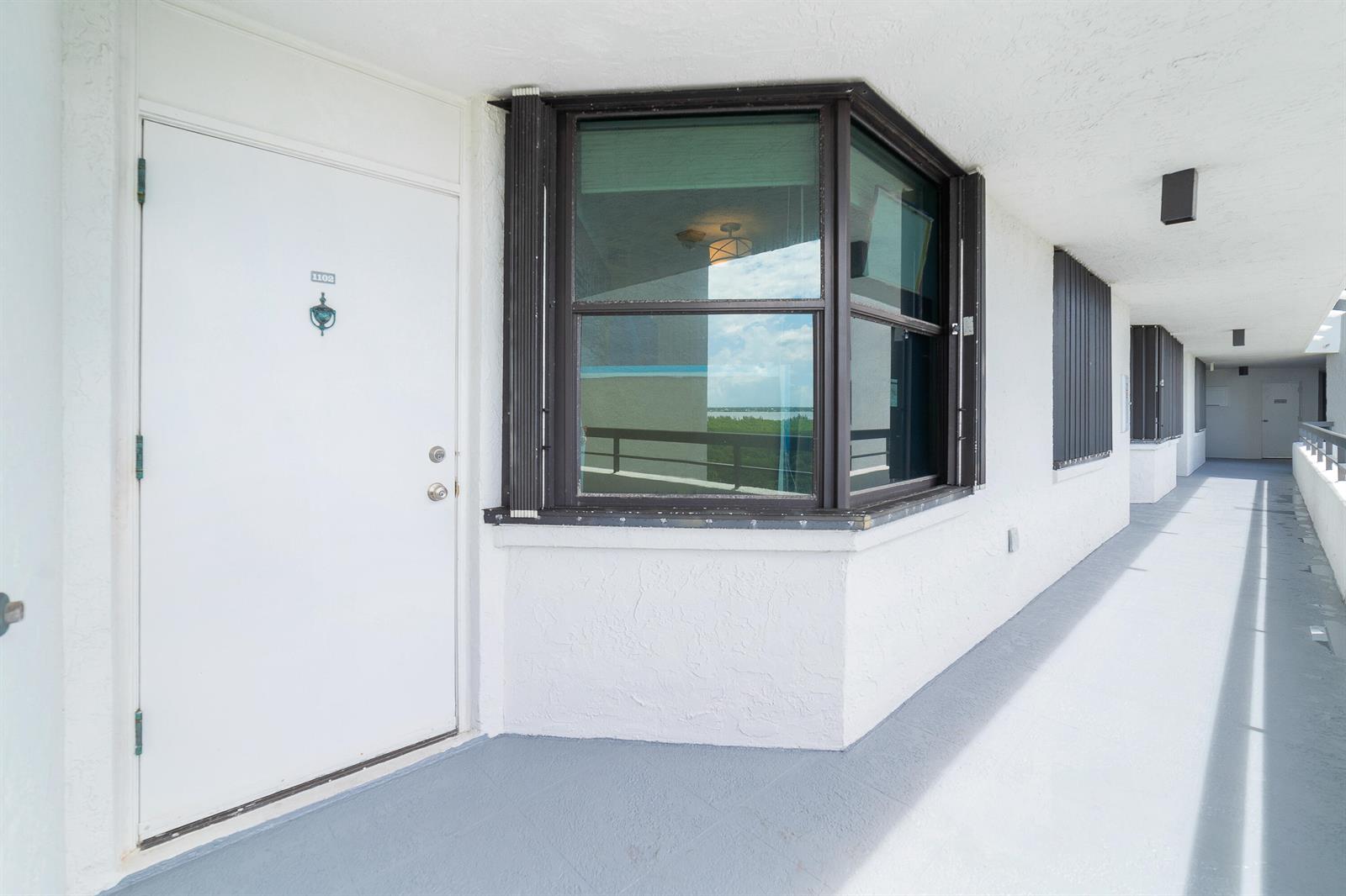 An exterior view of a white apartment door and a bay window on a walkway — 8800 S Ocean Drive # 1102, Jensen Beach FL 34957, JENSEN BEACH, FL