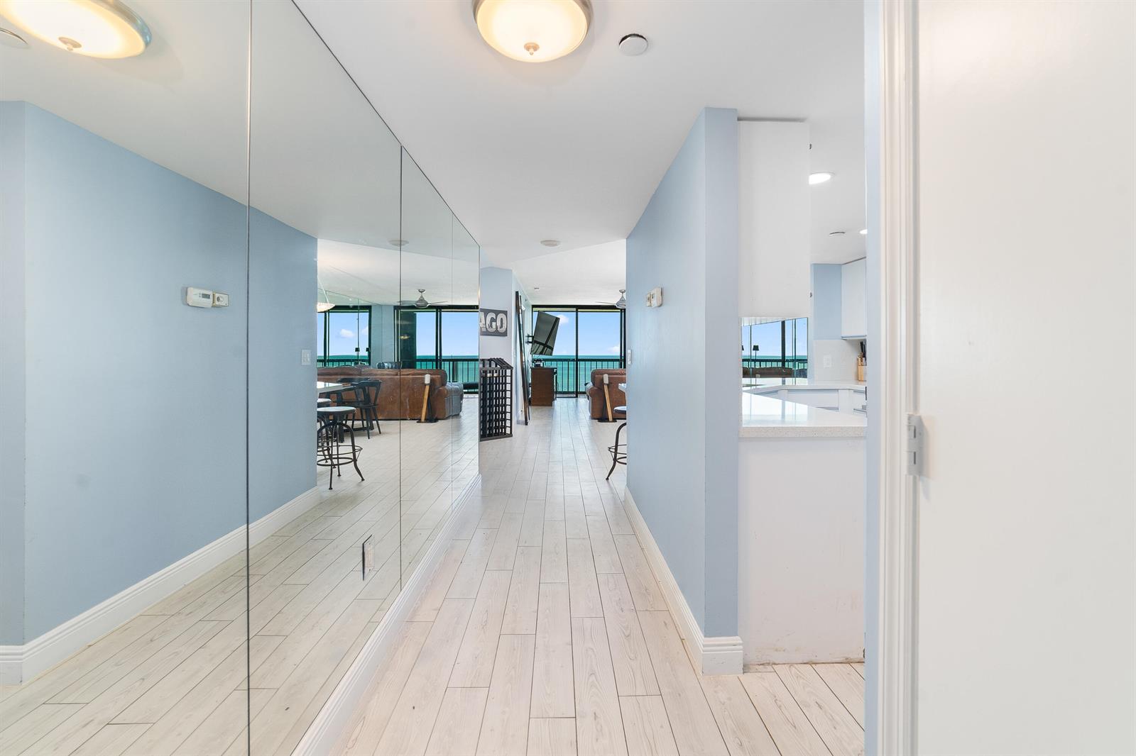 A hallway with light wood floors and a mirrored wall leads to an oceanfront living area — 8800 S Ocean Drive # 1102, Jensen Beach FL 34957, JENSEN BEACH, FL
