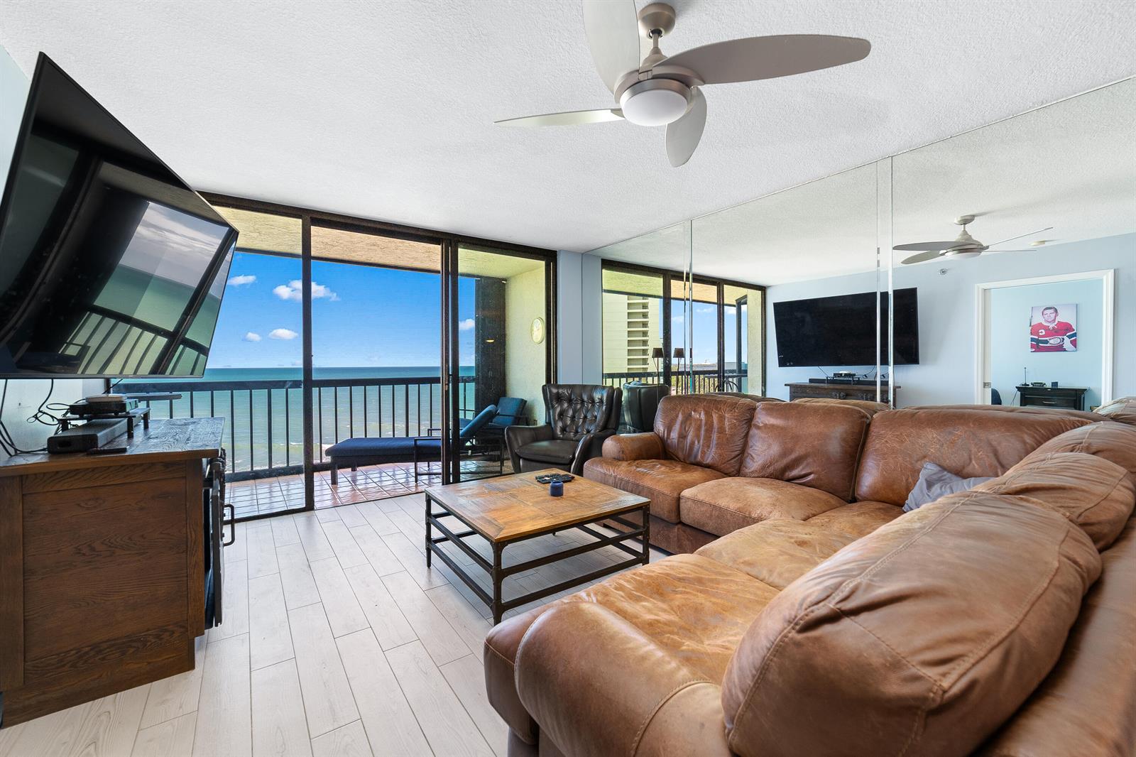 A living room with a leather sectional, wood coffee table, and balcony overlooking the ocean — 8800 S Ocean Drive # 1102, Jensen Beach FL 34957, JENSEN BEACH, FL